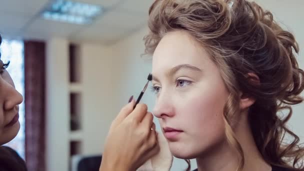 Maskér dělá profesionální make-up mladé ženy v studio krásy — Stock video