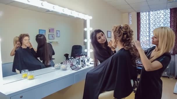 Kunstenaar doen professionele make-up make-up en haarstylist maakt kapsel van jonge vrouw — Stockvideo