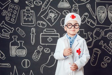 Mutlu küçük çocuk bir doktor desenli koyu arka plan üzerinde şırınga tutarak bardaklarda gibi