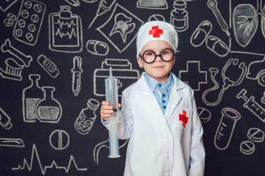 Mutlu küçük çocuk bir doktor desenli koyu arka plan üzerinde şırınga tutarak bardaklarda gibi