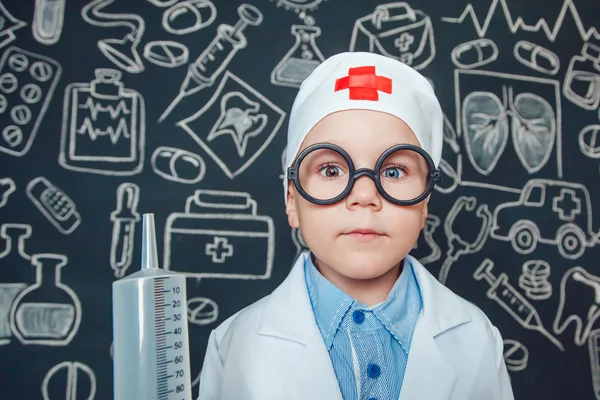 Niño feliz como médico en gafas con jeringa sobre fondo oscuro con patrón — Foto de Stock