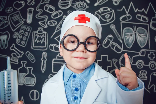 Mutlu küçük çocuk bir doktor desenli koyu arka plan üzerinde şırınga tutarak bardaklarda gibi