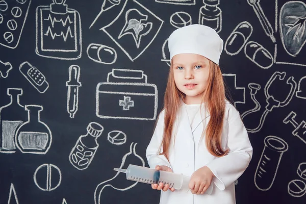 Klein meisje in dokter kostuum houden spuit op donkere achtergrond met patroon Rechtenvrije Stockafbeeldingen
