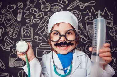 Şırınga ve sthetoscope desenli koyu arka plan üzerinde tutan doktor kostüm mutlu küçük çocuk. Çocuk bıyıkları, gözlük vardır