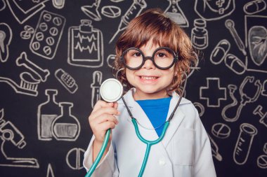 Sthetoscope desenli koyu arka plan üzerinde tutan doktor kostüm mutlu küçük çocuk. Çocuk gözlük vardır
