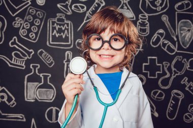 Sthetoscope desenli koyu arka plan üzerinde tutan doktor kostüm mutlu küçük çocuk. Çocuk gözlük vardır
