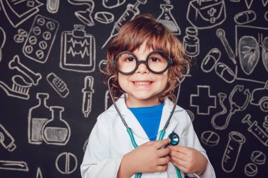 Sthetoscope desenli koyu arka plan üzerinde tutan doktor kostüm mutlu küçük çocuk. Çocuk gözlük vardır