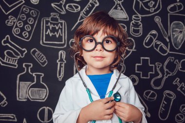 Sthetoscope desenli koyu arka plan üzerinde tutan doktor kostüm mutlu küçük çocuk. Çocuk gözlük vardır