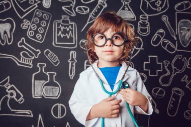 Sthetoscope desenli koyu arka plan üzerinde tutan doktor kostüm mutlu küçük çocuk. Çocuk gözlük vardır