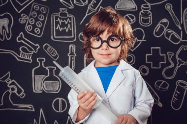 Mutlu küçük çocuk desenli koyu arka plan üzerinde şırınga tutarak doktor kostüm. Çocuk gözlük vardır