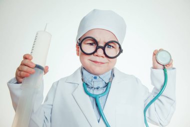 Doktor kostüm şırınga ve sthetoscope beyaz arka plan üzerinde tutarak gözlüklü mutlu küçük çocuk.
