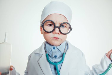 Doktor kostüm şırınga ve sthetoscope beyaz arka plan üzerinde tutarak gözlüklü mutlu küçük çocuk.