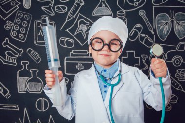Şırınga ve sthetoscope desenli koyu arka plan üzerinde tutan doktor kostüm mutlu küçük çocuk. Çocuk gözlük vardır