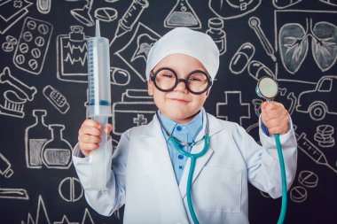 Şırınga ve sthetoscope desenli koyu arka plan üzerinde tutan doktor kostüm mutlu küçük çocuk. Çocuk gözlük vardır