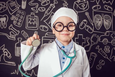 Sthetoscope desenli koyu arka plan üzerinde tutan doktor kostüm mutlu küçük çocuk. Çocuk gözlük vardır