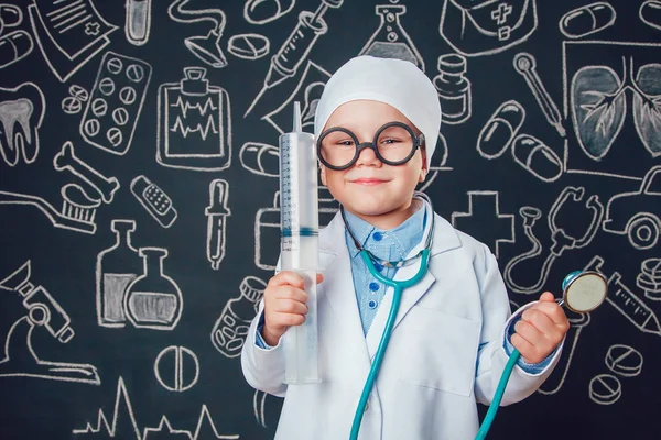 Şırınga ve sthetoscope desenli koyu arka plan üzerinde tutan doktor kostüm mutlu küçük çocuk. Çocuk gözlük vardır