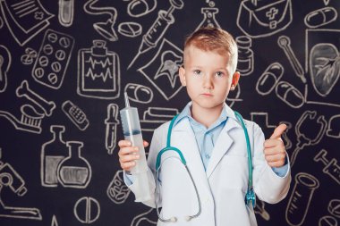 Doktor kostüm şırınga ve gösterir sınıf desenli koyu arka plan üzerinde tutan küçük çocuk.