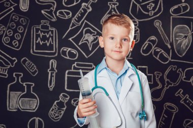 Mutlu küçük çocuk desenli koyu arka plan üzerinde şırınga tutarak doktor kostüm.
