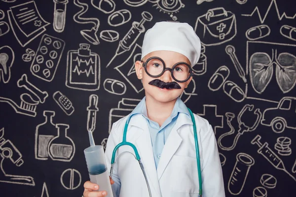 Little boy in doctor costume holding syringe on dark background with pattern. The child has mustache and glasses — Stock Photo, Image