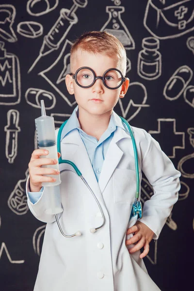 Doktor kostüm şırınga desenli koyu arka plan üzerinde tutan küçük bir çocuk. Çocuk gözlük vardır