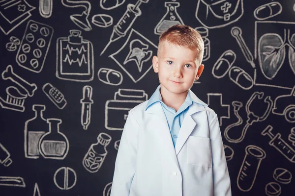 Little boy in doctor costume standing on dark background with pattern. — Stock Photo, Image