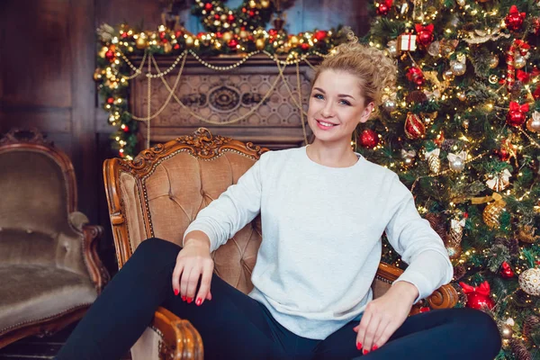 Junge hübsche blonde Frau sitzt auf einem Stuhl in der Nähe des Weihnachtsbaums. Neues Jahr — Stockfoto