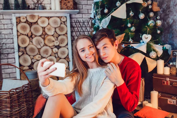 Young couple in love sitting near christmas tree having fun and make selfie. New Year — Stock Photo, Image