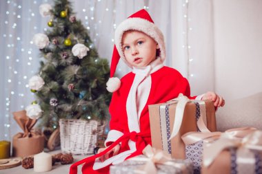 Noel Baba hediyeleri Noel dekorasyonu ile oturan küçük çocuk kılığında. Yeni yıl.