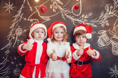 Çocuklar Noel Baba Noel desenli koyu arka plan üzerinde ayakta ve gösteri başparmak gibi giyinmiş. Yeni yıl.