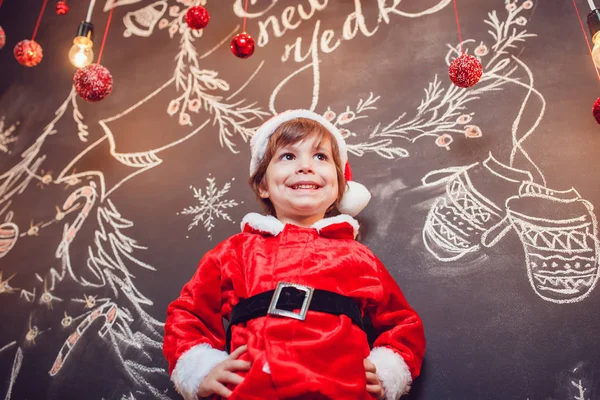 Petit garçon habillé en Père Noël debout sur fond sombre avec motif de Noël. Nouvel An . — Photo