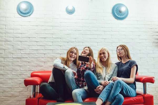 Vakre jenter som sitter på sofaen, har det gøy og lager selfie på Hostel – stockfoto