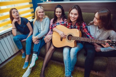 Güzel kızlar oturan kanepe, eğlenmek ve hosteli gitar çalmak.