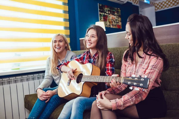 Schöne Mädchen sitzen auf der Couch, haben Spaß und spielen Gitarre im Hostel. — Stockfoto