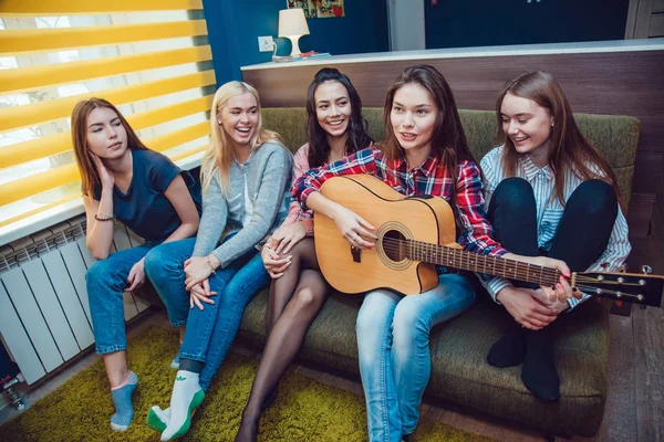 Schöne Mädchen sitzen auf der Couch, haben Spaß und spielen Gitarre im Hostel. — Stockfoto