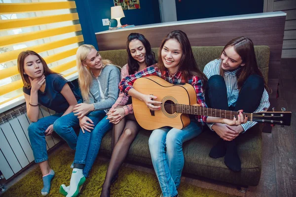 Vakre jenter sitter på sofaen, har det gøy og spiller gitar i Hostel . – stockfoto