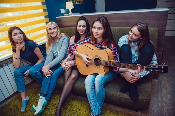 Beautiful girls sitting on couch, have fun and play the guitar in Hostel.