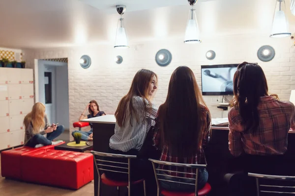 Hermosas chicas sentadas en el bar en el albergue, viendo la televisión y hablar . — Foto de Stock