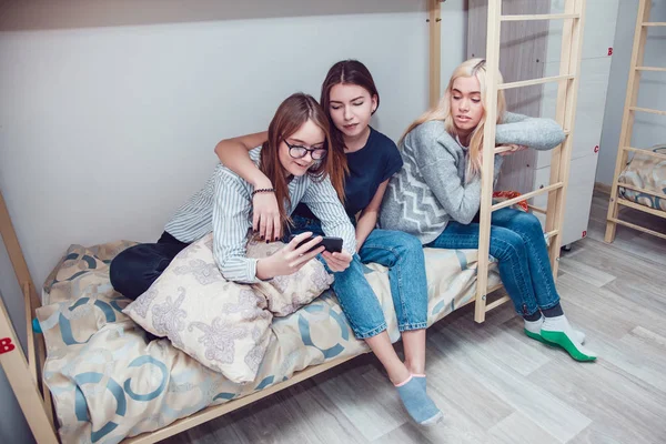 Gyönyörű lány ült egy ágyon a beszéd hostel, és használ smartphone. — Stock Fotó