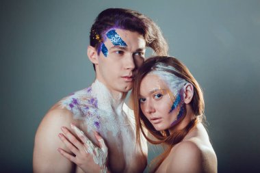 Moda genç adam ve kadın gri arka plan üzerinde yaratıcı yüz sanatı ile.