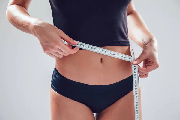 Atlético mulher magro medindo sua cintura por fita métrica no fundo branco — Fotografia de Stock