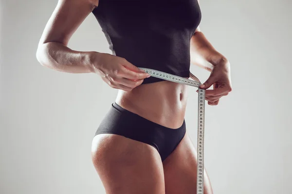 Atlética mujer delgada midiendo su cintura por cinta métrica sobre fondo blanco — Foto de Stock