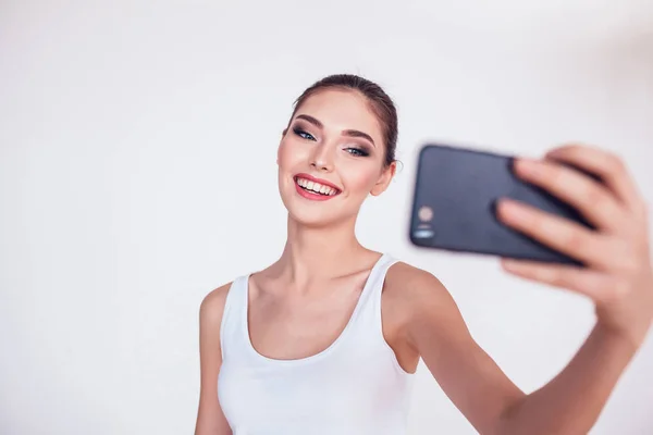 Hermosa chica morena con maquillaje hacer selfie sobre fondo blanco . — Foto de Stock