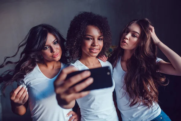 Trzy beautyful uśmiechniętych dziewcząt w biały t-shirt grymas i zrobić autoportret za pomocą smartfona. — Zdjęcie stockowe