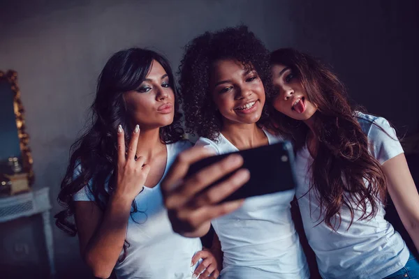 Trzy beautyful uśmiechniętych dziewcząt w biały t-shirt grymas i zrobić autoportret za pomocą smartfona. — Zdjęcie stockowe