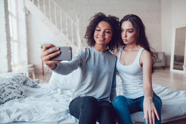 Piękne dziewczyny zrobić selfie, siedząc na łóżku w domu. — Zdjęcie stockowe
