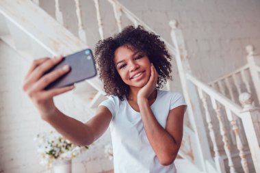 Beyaz t-shirt Beautyful Afrikalı kız olun smartphone evde kullanma selfie.