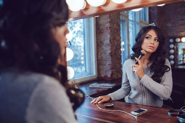 Hermosa mujer haciendo maquillaje mirando al espejo cerca de una ventana . — Foto de Stock