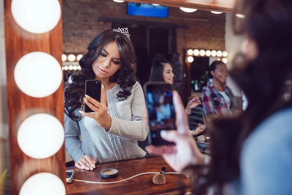 Hermosa mujer después del maquillaje mirando al espejo y hacer selfie en el estudio de belleza . — Foto de Stock