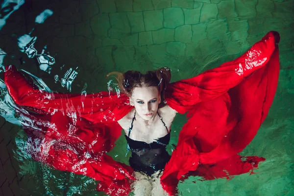 Mode kvinna med vackra professional utgör flytande i en pool av rött tyg. — Stockfoto