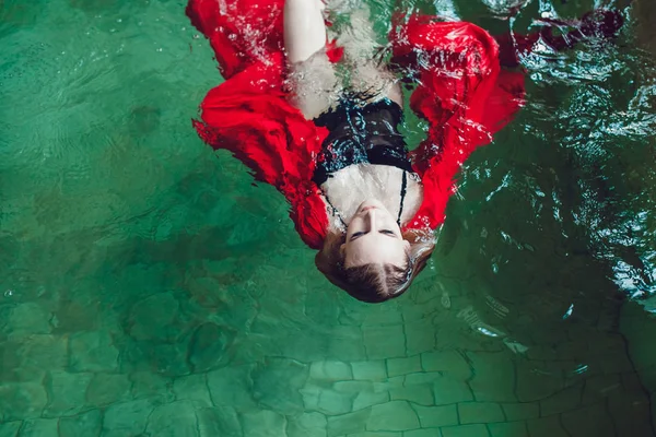 Mujer de moda con hermoso maquillaje profesional flotando en una piscina de tela roja . —  Fotos de Stock